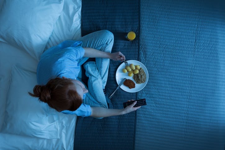 woman sitting  and eating dinner before going to bed, and holding a remote control