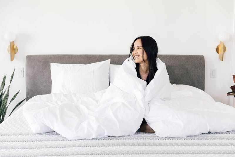 a_lady_smiling_in_a_leesa_mattress_wrapped_up_in_a_white_comforter