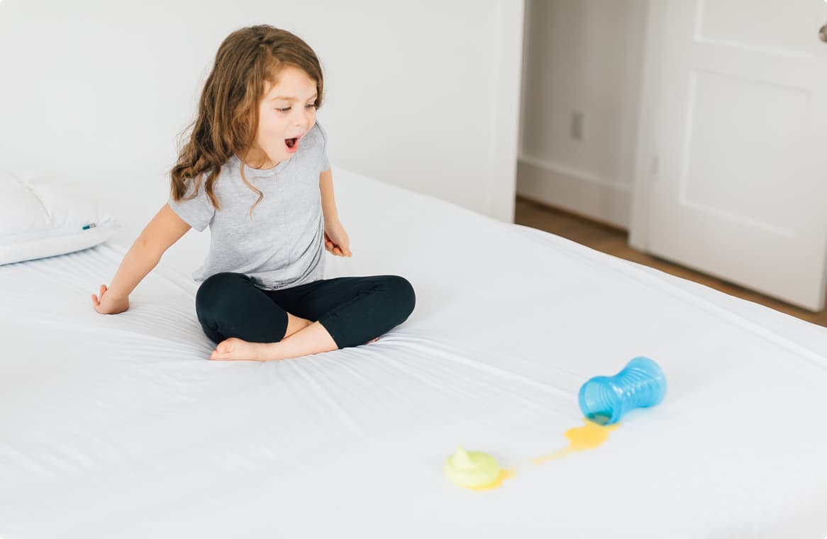 child spilling a drink on a mattress protector
