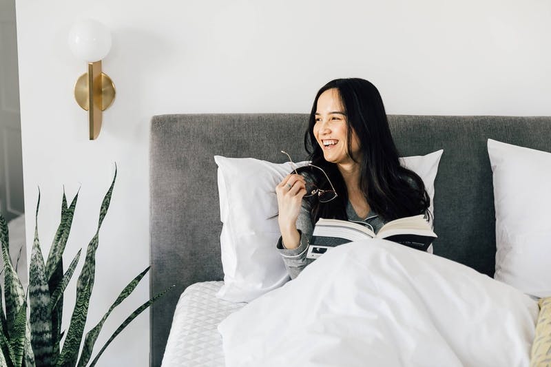 a_lady_reading_a_book_and_smiling_in_a_leesa_bed_gray_and_white