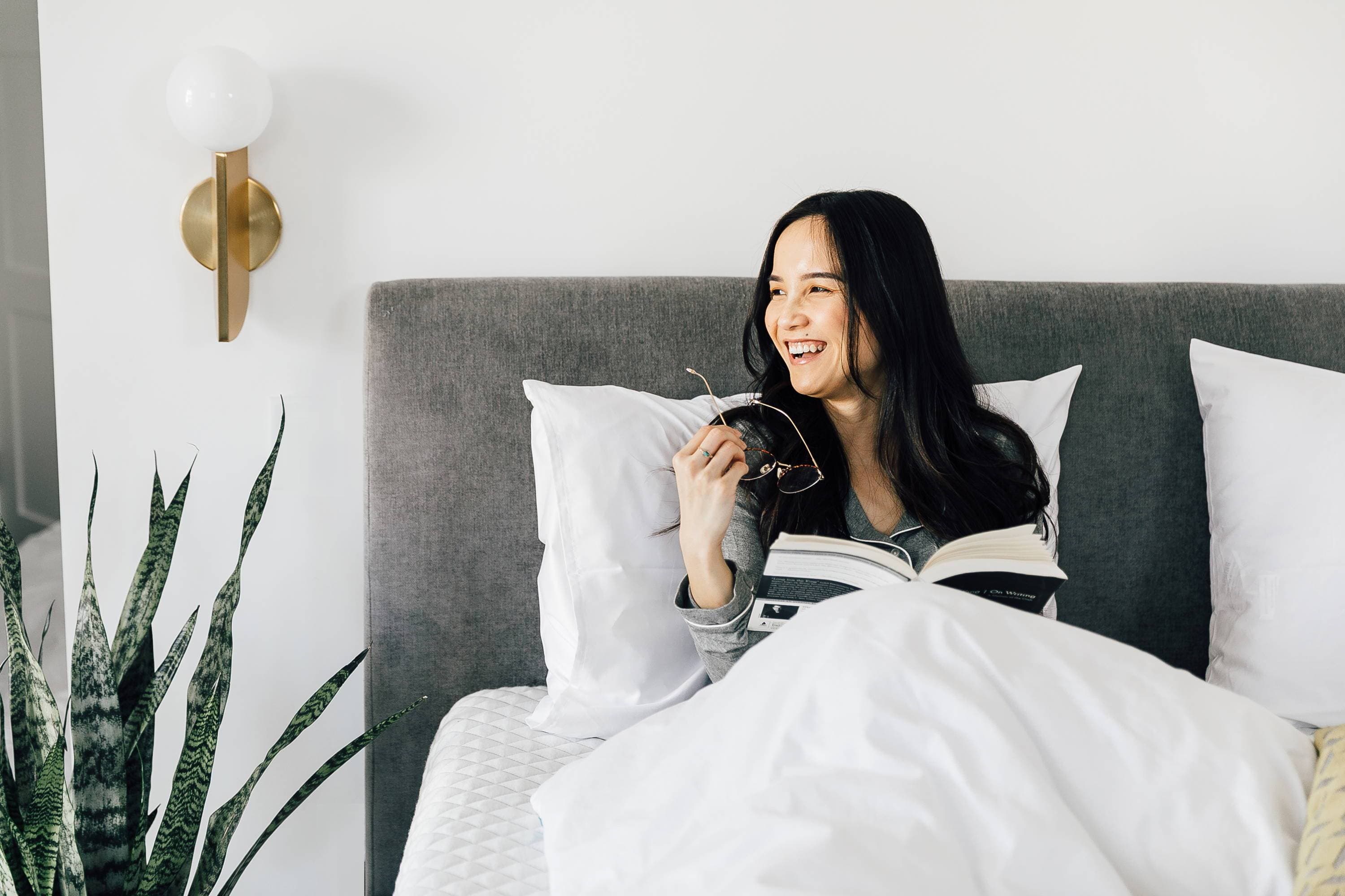 A lady smiling in a Leesa bed while reading