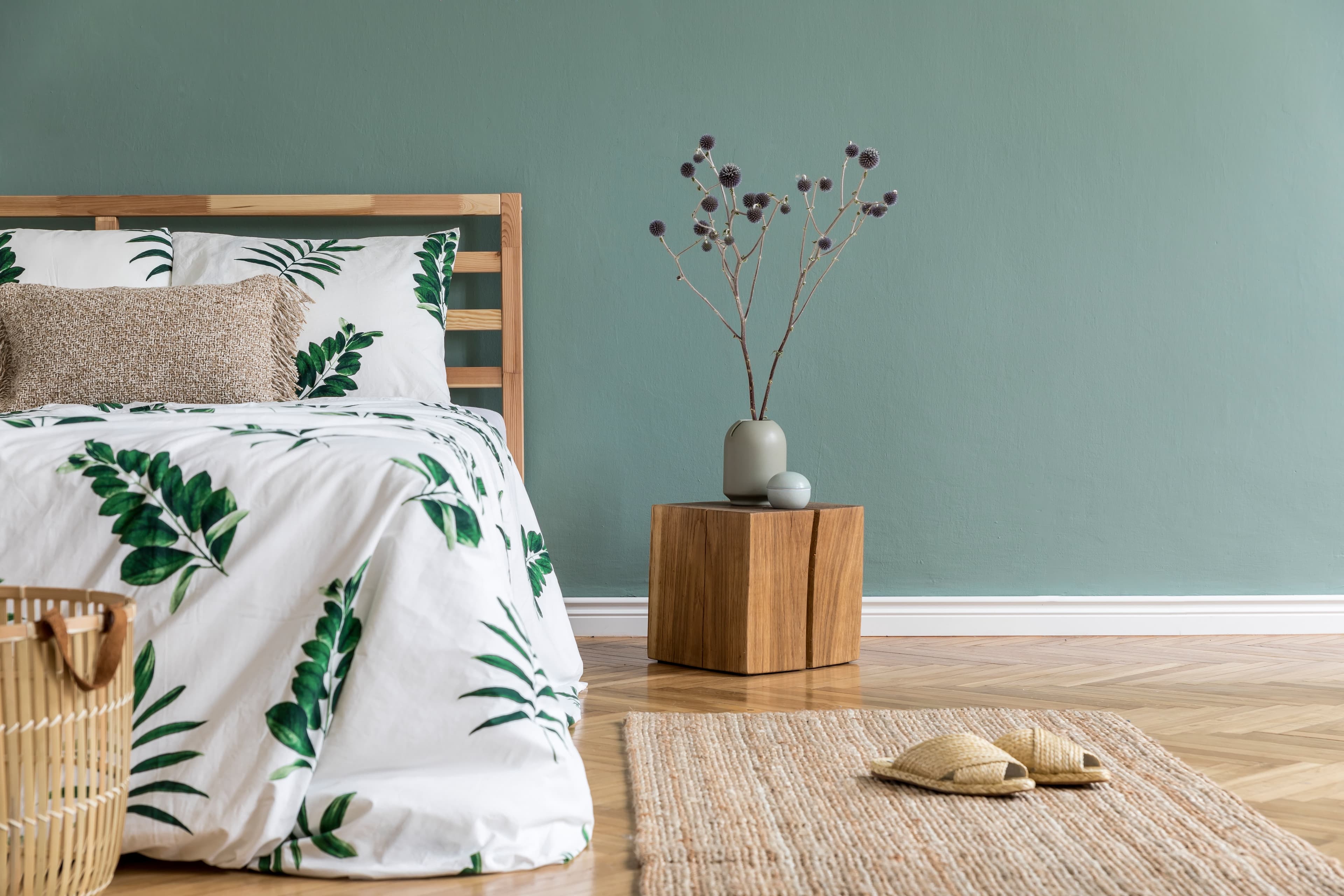 A calm green bedroom with bed that has wooden bed frame and has palm leaf duvet sheet design.